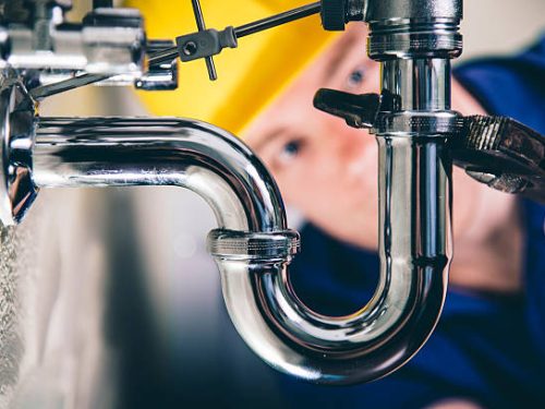 Plumber fixing a drain with adjustable wrench. Focus on drain, plumber defocused in back.